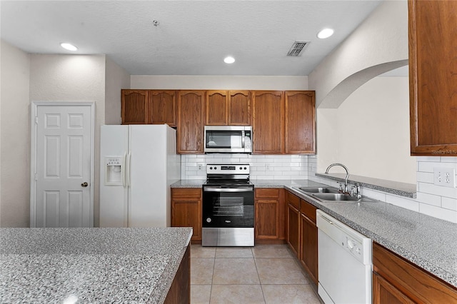 kitchen with visible vents, brown cabinetry, stainless steel appliances, a sink, and light tile patterned flooring