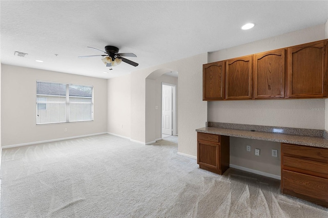 interior space featuring arched walkways, visible vents, light carpet, built in study area, and baseboards