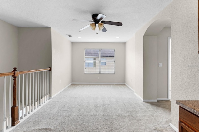 spare room featuring baseboards, visible vents, arched walkways, light colored carpet, and a textured ceiling