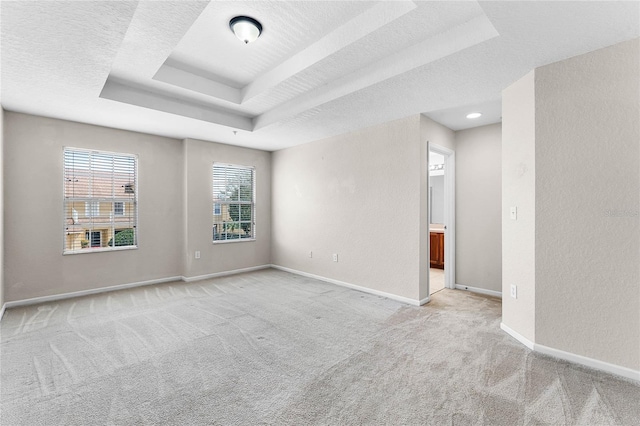 empty room with a textured ceiling, a tray ceiling, light colored carpet, and baseboards