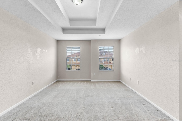 spare room featuring baseboards, light colored carpet, a textured wall, a tray ceiling, and a textured ceiling