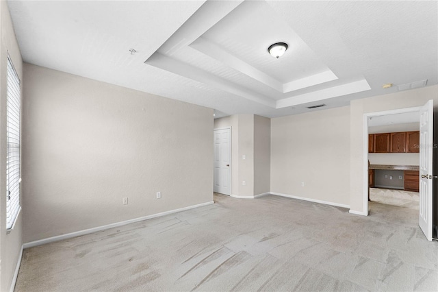 interior space with a tray ceiling, light colored carpet, visible vents, a healthy amount of sunlight, and baseboards