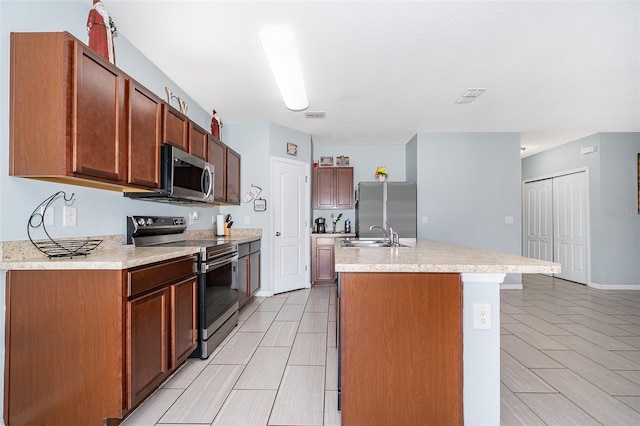 kitchen featuring a kitchen island with sink, stainless steel appliances, a sink, visible vents, and light countertops