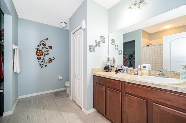 full bath featuring toilet, vanity, baseboards, a spacious closet, and walk in shower