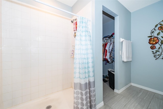 bathroom with a shower stall, a spacious closet, and baseboards