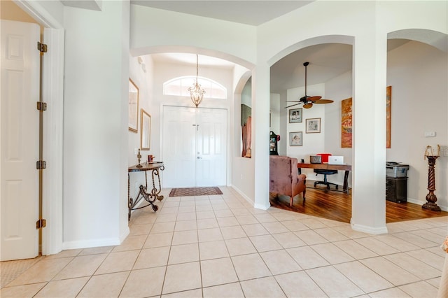 foyer with ceiling fan with notable chandelier, light tile patterned flooring, and baseboards