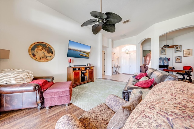 living area with arched walkways, visible vents, a high ceiling, a ceiling fan, and wood finished floors