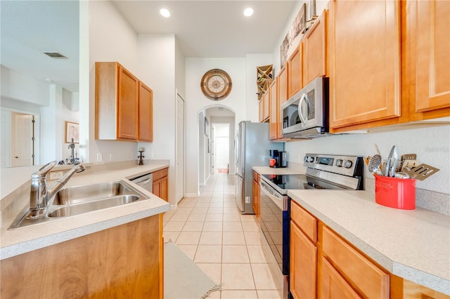 kitchen featuring arched walkways, light tile patterned floors, a sink, light countertops, and appliances with stainless steel finishes