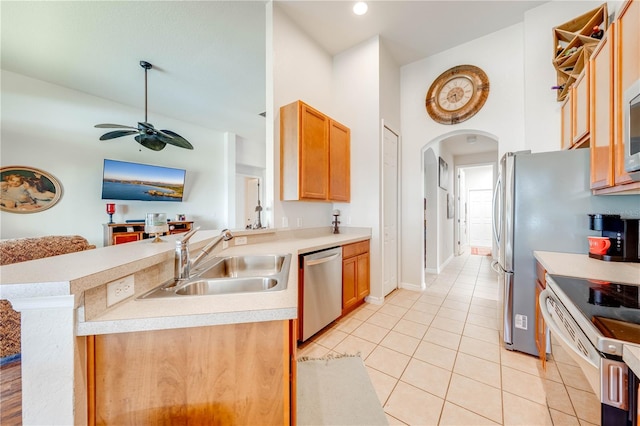 kitchen featuring arched walkways, a peninsula, a sink, light countertops, and appliances with stainless steel finishes