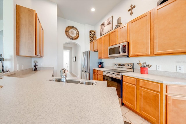 kitchen with light tile patterned floors, arched walkways, appliances with stainless steel finishes, light countertops, and a sink