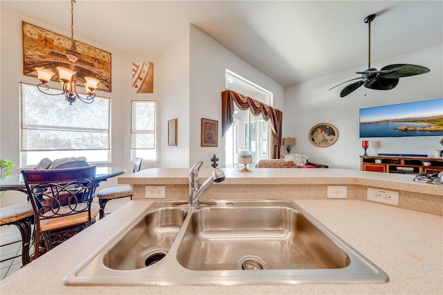 kitchen with light countertops, hanging light fixtures, open floor plan, a sink, and ceiling fan with notable chandelier