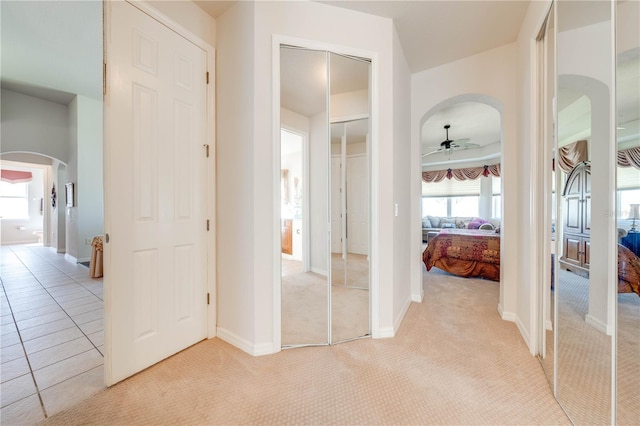 corridor with arched walkways, light colored carpet, and baseboards