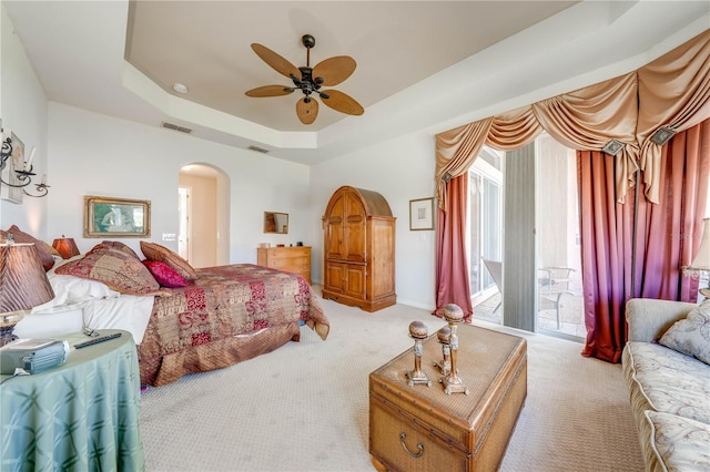 carpeted bedroom featuring visible vents, a raised ceiling, arched walkways, ceiling fan, and access to outside