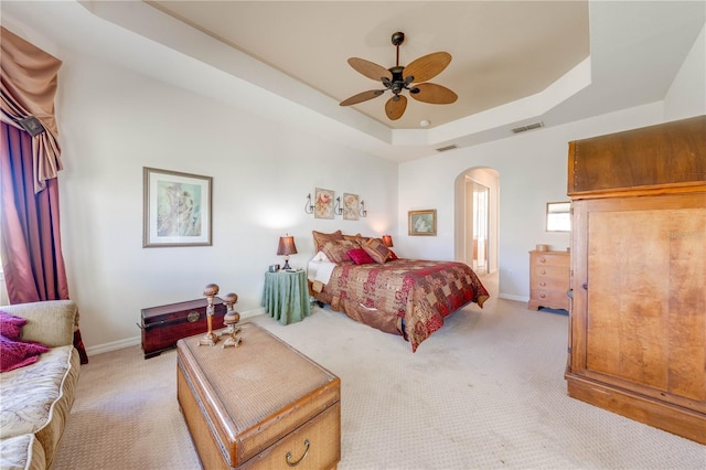 bedroom featuring a tray ceiling, arched walkways, visible vents, light carpet, and baseboards