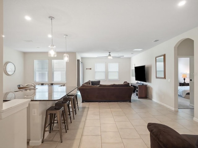 living area featuring arched walkways, ceiling fan, light tile patterned flooring, and baseboards