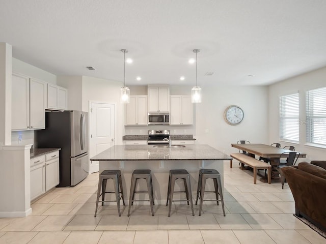 kitchen featuring stainless steel appliances, visible vents, a kitchen island with sink, a sink, and a kitchen breakfast bar