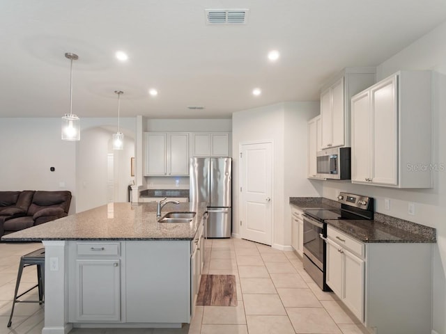 kitchen with visible vents, dark stone countertops, stainless steel appliances, a kitchen bar, and a sink