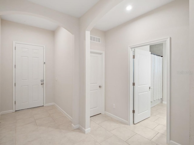 hall featuring light tile patterned floors, baseboards, visible vents, and arched walkways