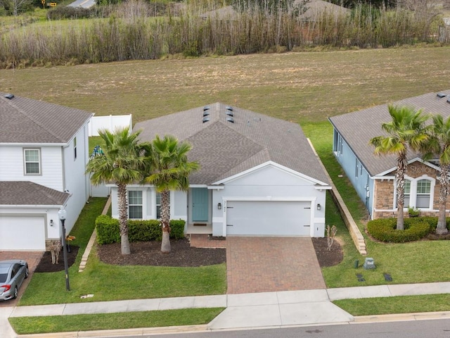 view of front of house with a shingled roof, an attached garage, decorative driveway, a front lawn, and stucco siding