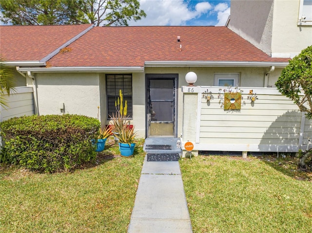 view of front facade featuring a front lawn, roof with shingles, and stucco siding