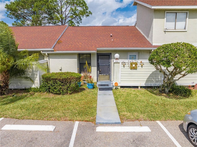 view of front of property featuring a front yard, uncovered parking, roof with shingles, and stucco siding