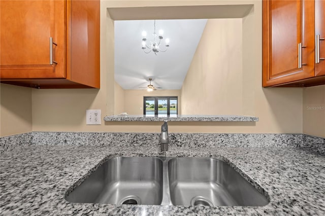 kitchen view of a sink, brown cabinets, light stone countertops, and a chandelier