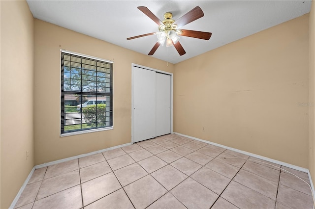 unfurnished bedroom featuring a closet, light tile patterned floors, baseboards, and ceiling fan