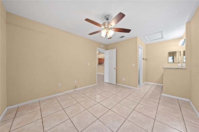 empty room featuring light tile patterned floors, a ceiling fan, baseboards, and attic access