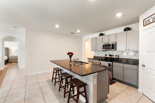 kitchen featuring arched walkways, stainless steel appliances, a sink, gray cabinets, and decorative backsplash