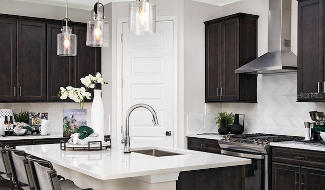 kitchen with a breakfast bar, light countertops, stainless steel gas stove, a sink, and wall chimney range hood