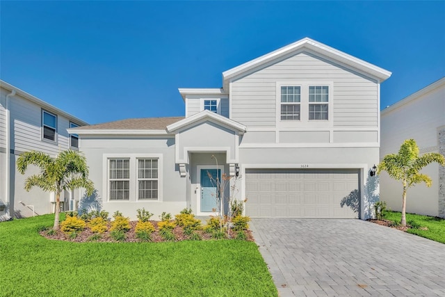 traditional home with a front lawn, decorative driveway, an attached garage, and stucco siding