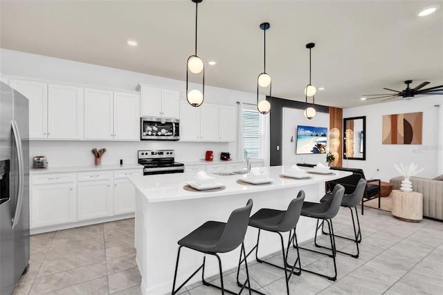 kitchen with a kitchen island with sink, stainless steel appliances, light countertops, a kitchen bar, and white cabinetry