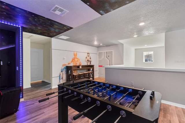 rec room featuring visible vents, a textured ceiling, baseboards, and wood finished floors