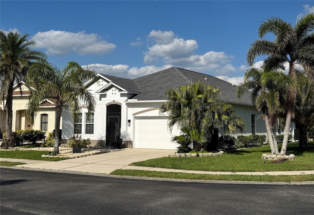 view of front facade featuring an attached garage, concrete driveway, roof with shingles, stucco siding, and a front yard