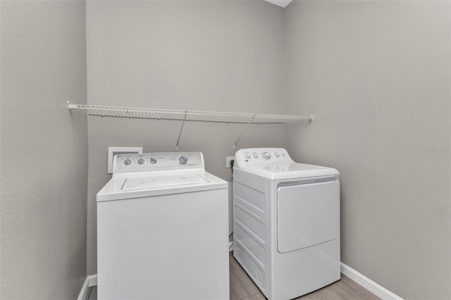 clothes washing area with light wood finished floors, washer and clothes dryer, laundry area, and baseboards