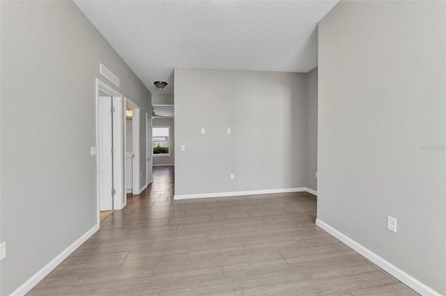 unfurnished room featuring baseboards, visible vents, and a textured ceiling