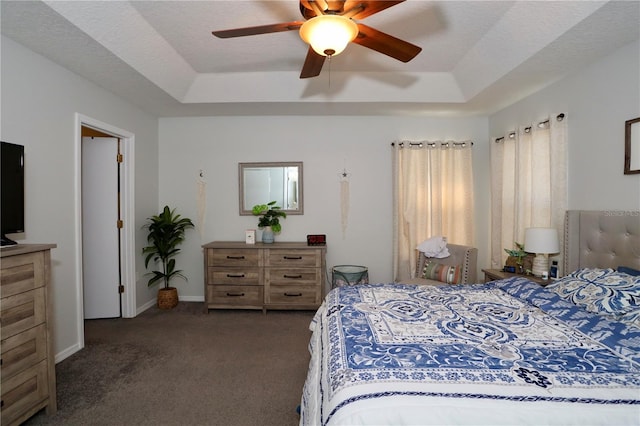 bedroom featuring a textured ceiling, baseboards, a tray ceiling, and dark colored carpet