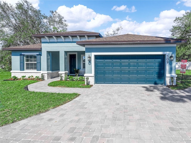 prairie-style home featuring decorative driveway, an attached garage, a front yard, and stucco siding