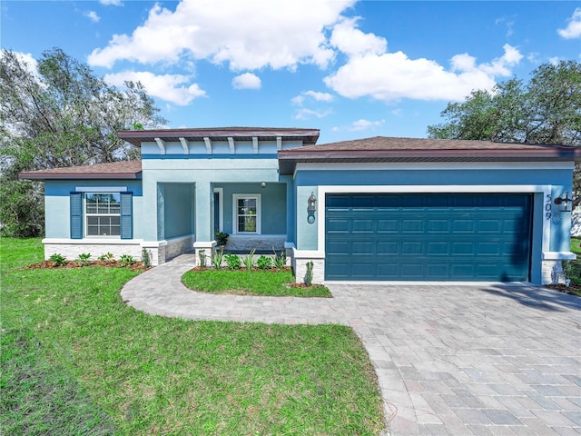 prairie-style home featuring a garage, decorative driveway, a front lawn, and stucco siding