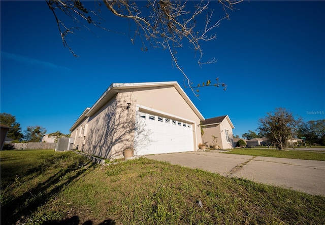 view of side of home featuring stucco siding, a yard, central AC unit, and driveway