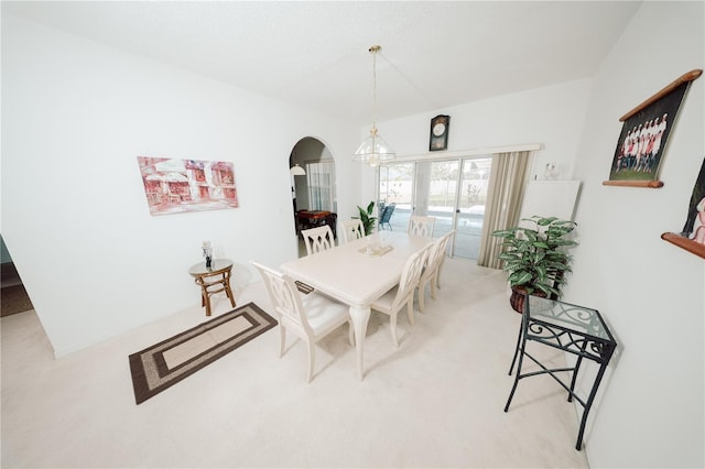 dining space with light colored carpet, arched walkways, and a chandelier