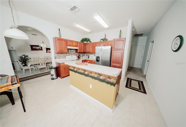 kitchen featuring stove, visible vents, under cabinet range hood, and stainless steel fridge with ice dispenser