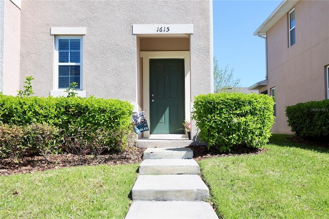 doorway to property with a lawn and stucco siding