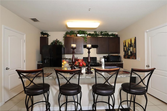 kitchen with visible vents, a kitchen bar, dark brown cabinetry, and black appliances