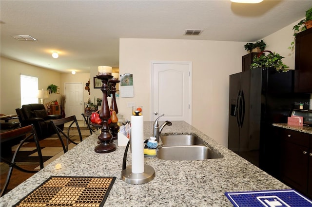 kitchen with visible vents, a sink, light stone counters, black fridge with ice dispenser, and dark brown cabinets