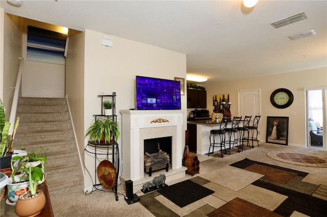 living area featuring visible vents, a fireplace with raised hearth, and stairs