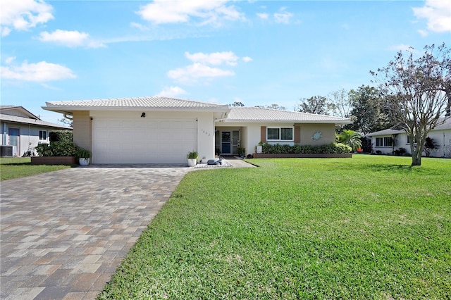 ranch-style house featuring an attached garage, a tiled roof, decorative driveway, stucco siding, and a front lawn