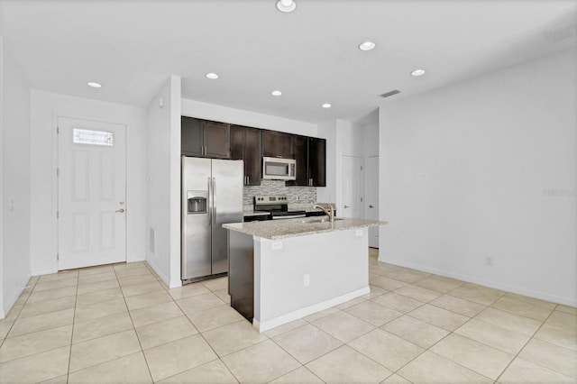 kitchen with stainless steel appliances, visible vents, decorative backsplash, an island with sink, and light stone countertops