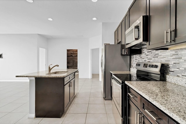 kitchen with tasteful backsplash, appliances with stainless steel finishes, a kitchen island with sink, light tile patterned flooring, and a sink