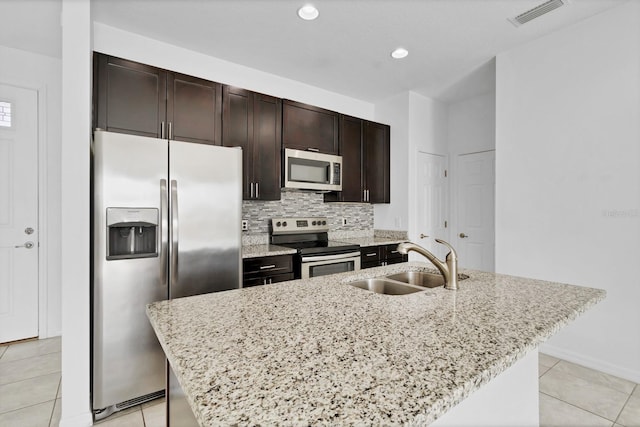 kitchen with tasteful backsplash, a center island with sink, appliances with stainless steel finishes, dark brown cabinets, and a sink